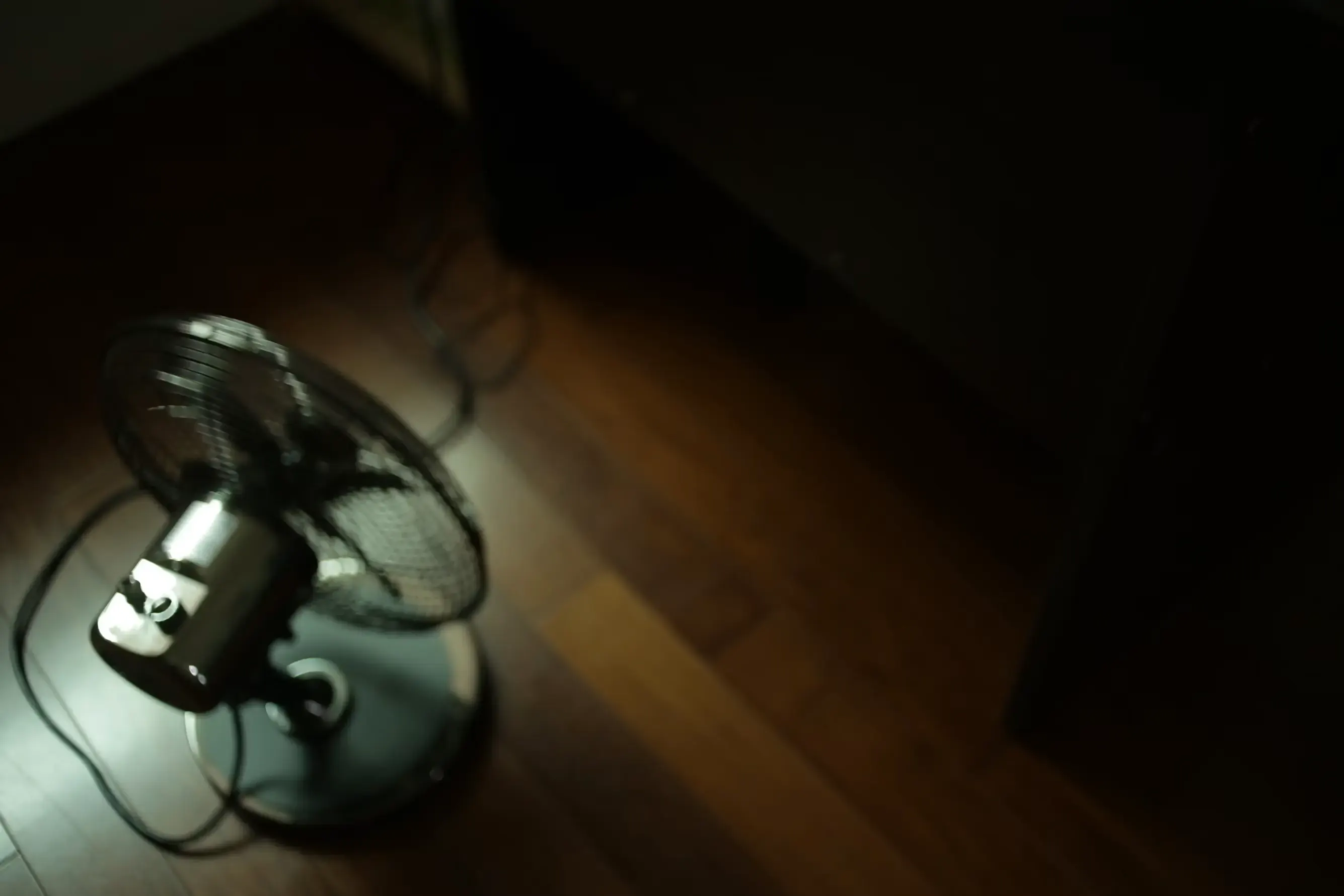 Un ventilatore da tavolo nero e grigio appoggiato su un pavimento in parquet di legno marrone.