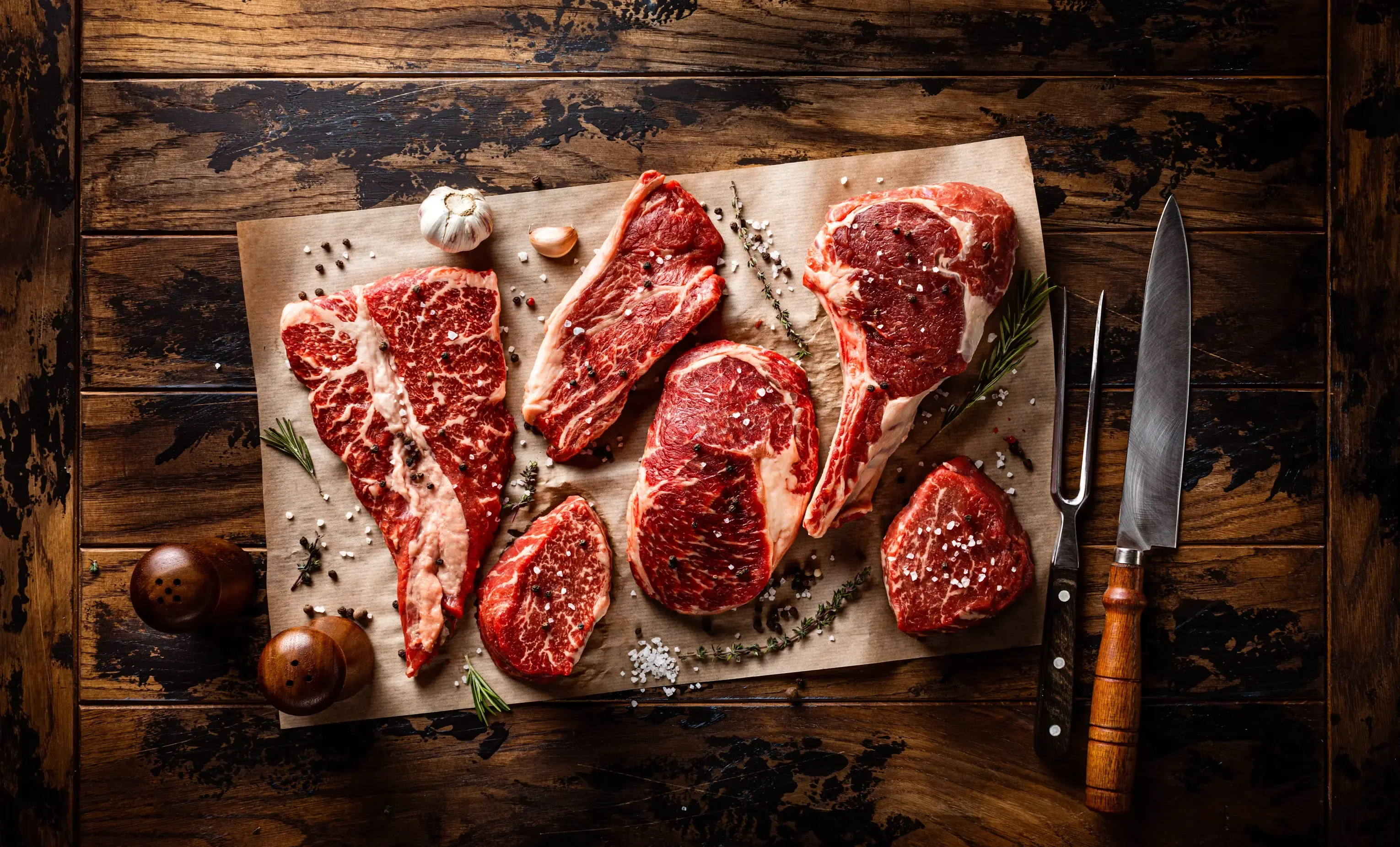 Piezas de carne cruda sobre una tabla de cortar de madera, junto a un cuchillo de cocina.