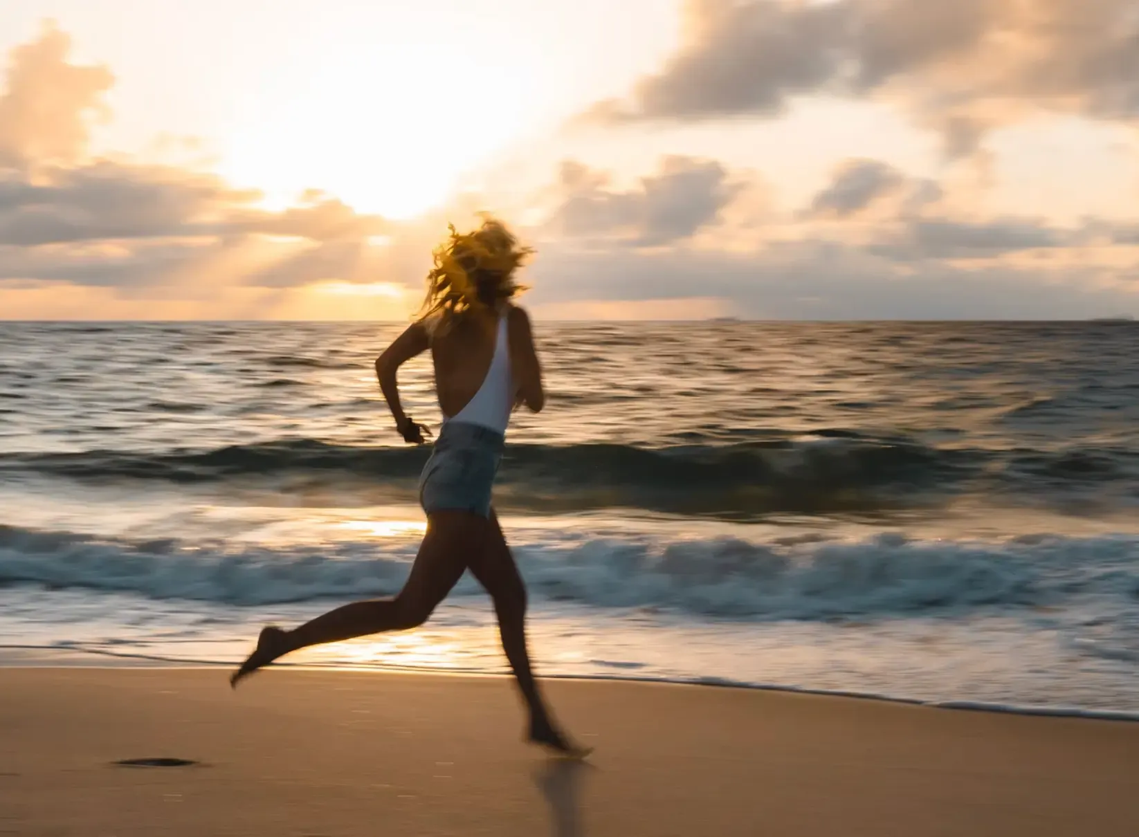 Una persona che corre scalza sulla riva di una spiaggia all'alba.