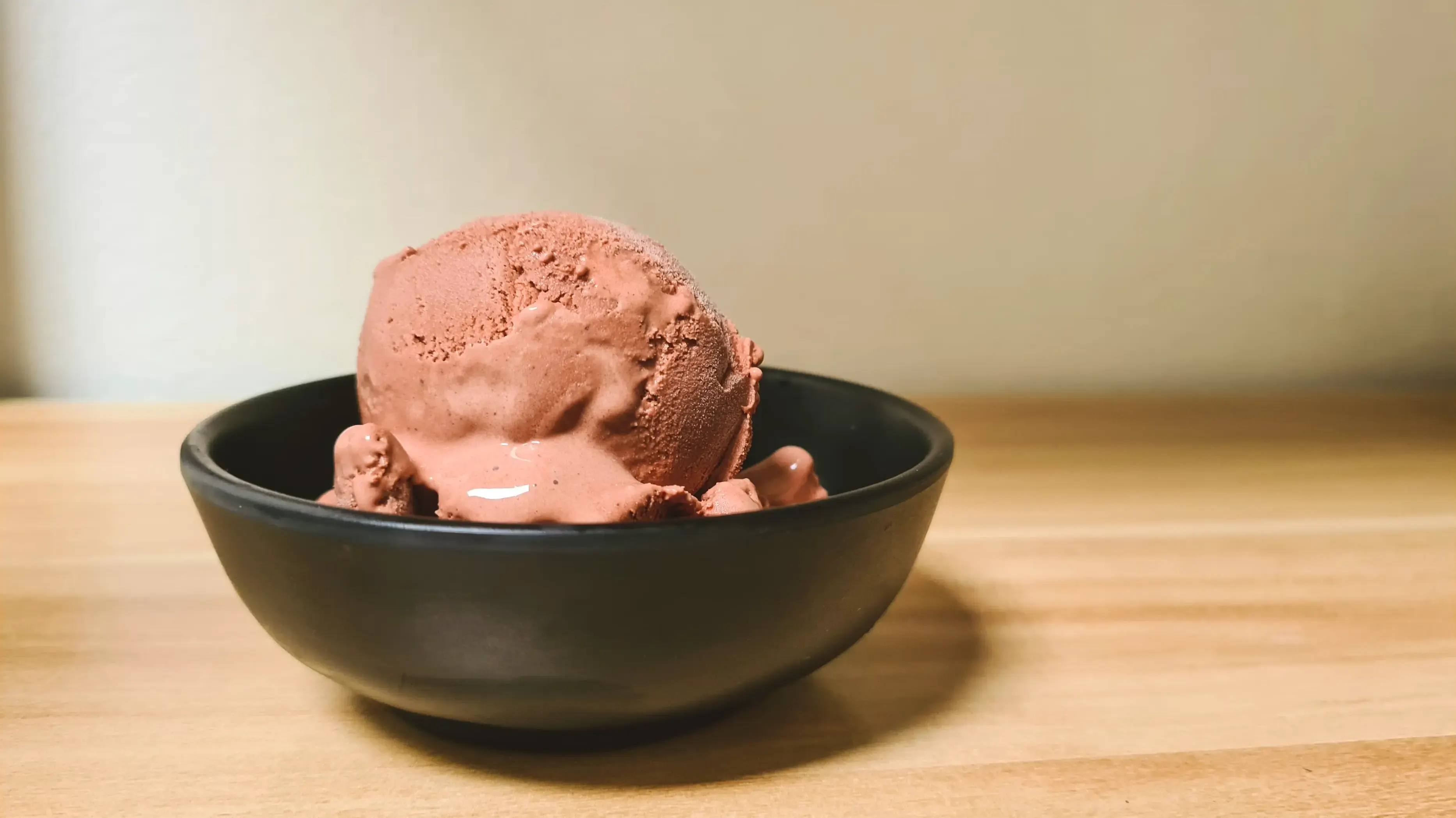 Una pallina di gelato al cioccolato che inizia a sciogliersi in una ciotola di ceramica nera.